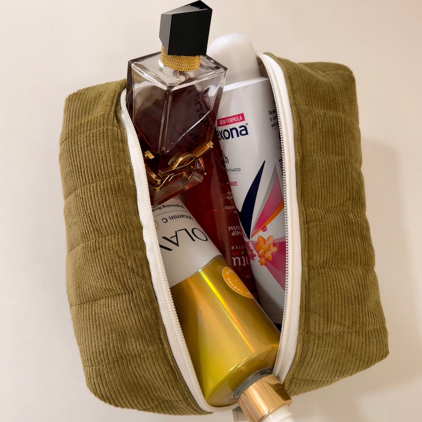 Green toiletry bag with various products including a bottle and a can on a beige background