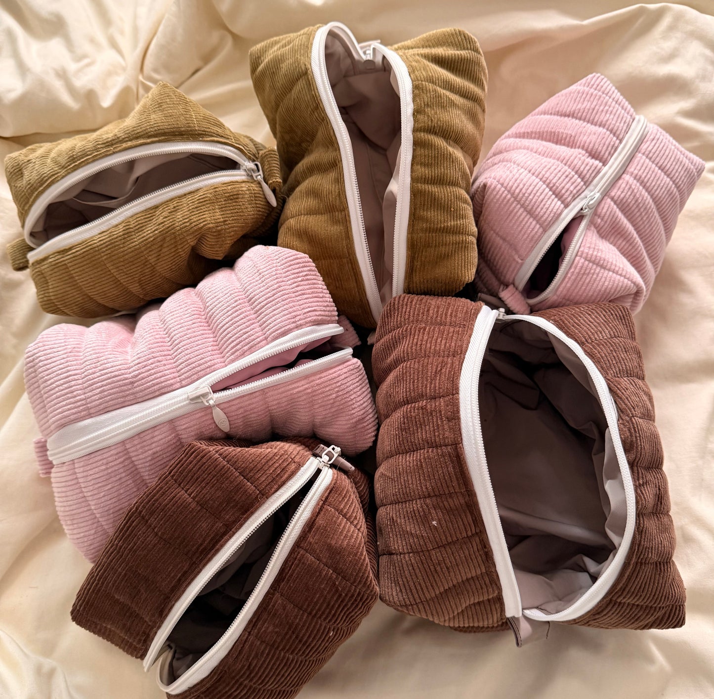 Folded corduroy robes in various colors on a soft beige fabric background