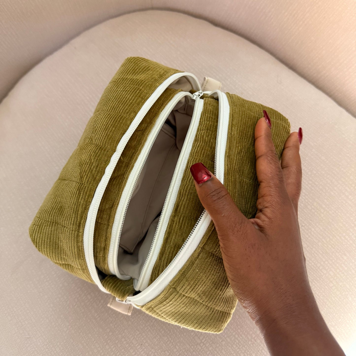 Green fabric pouch with white zippers held by a hand on a beige background