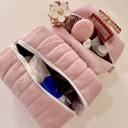 Pink textured makeup bag with cosmetic items on a light pink background