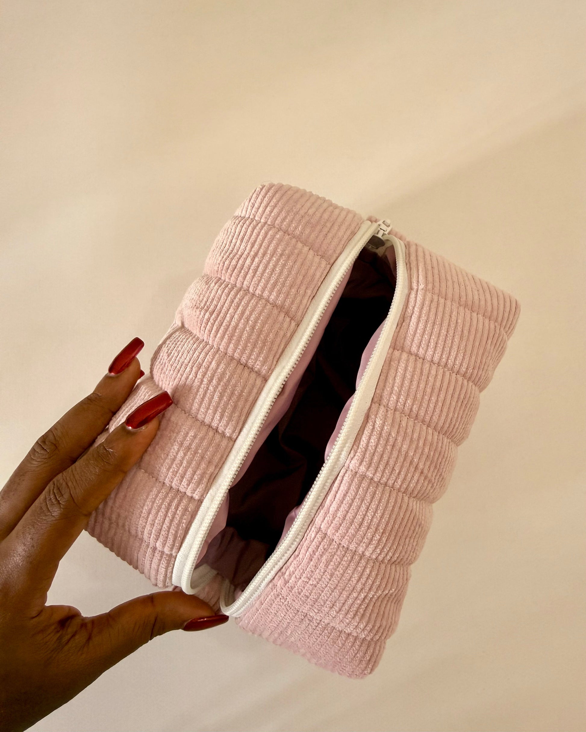 Pink textured pouch held by a hand against a beige background