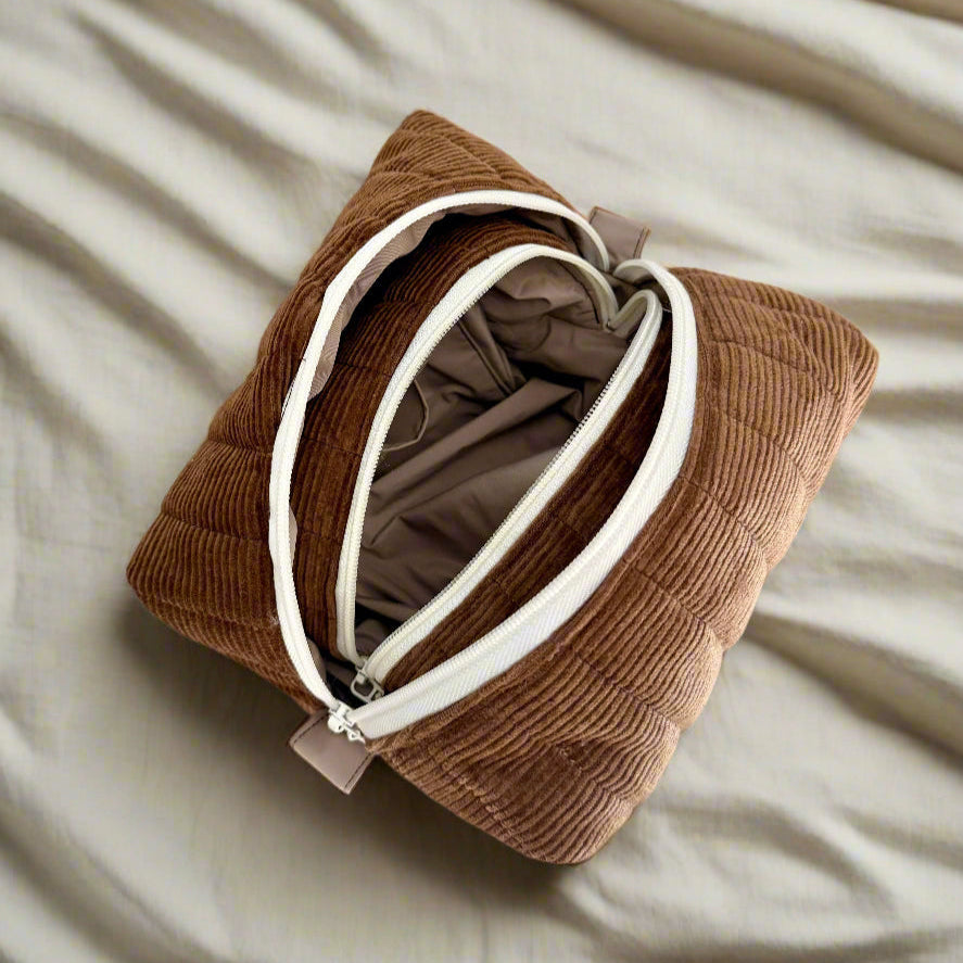 Brown corduroy pouch with a white zipper on a beige surface