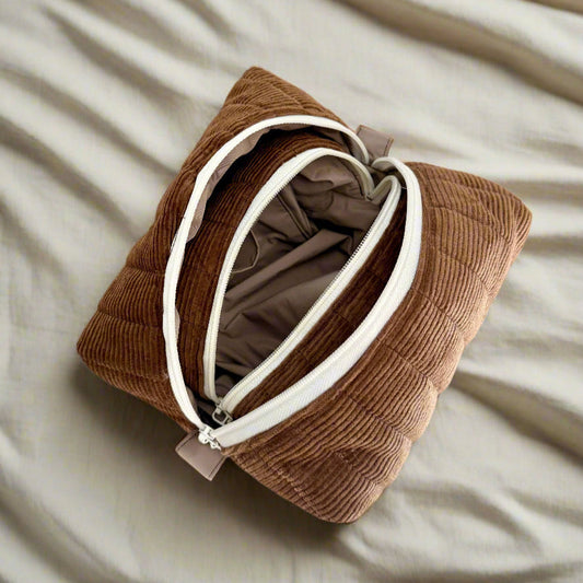 Brown corduroy pouch with a white zipper on a beige surface