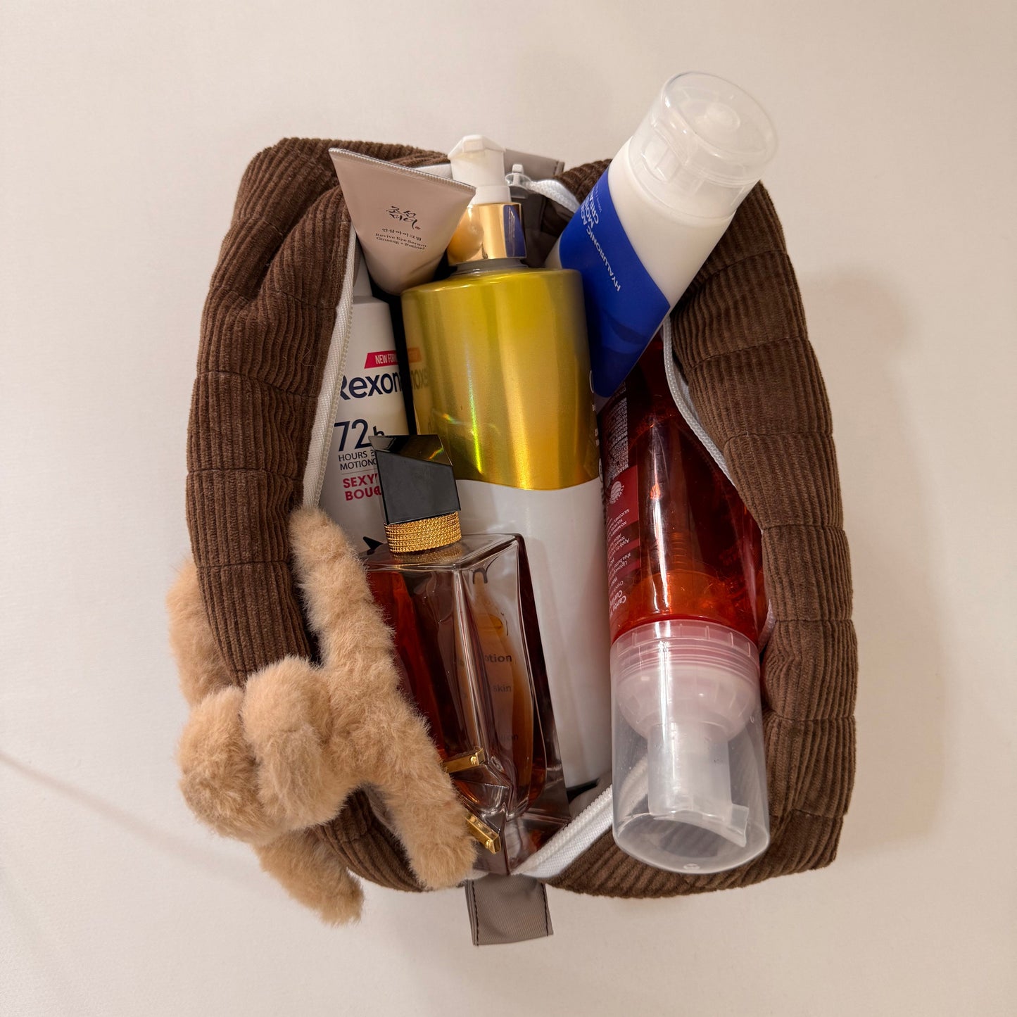 Pouch with various toiletries including bottles and a small teddy bear on a white surface