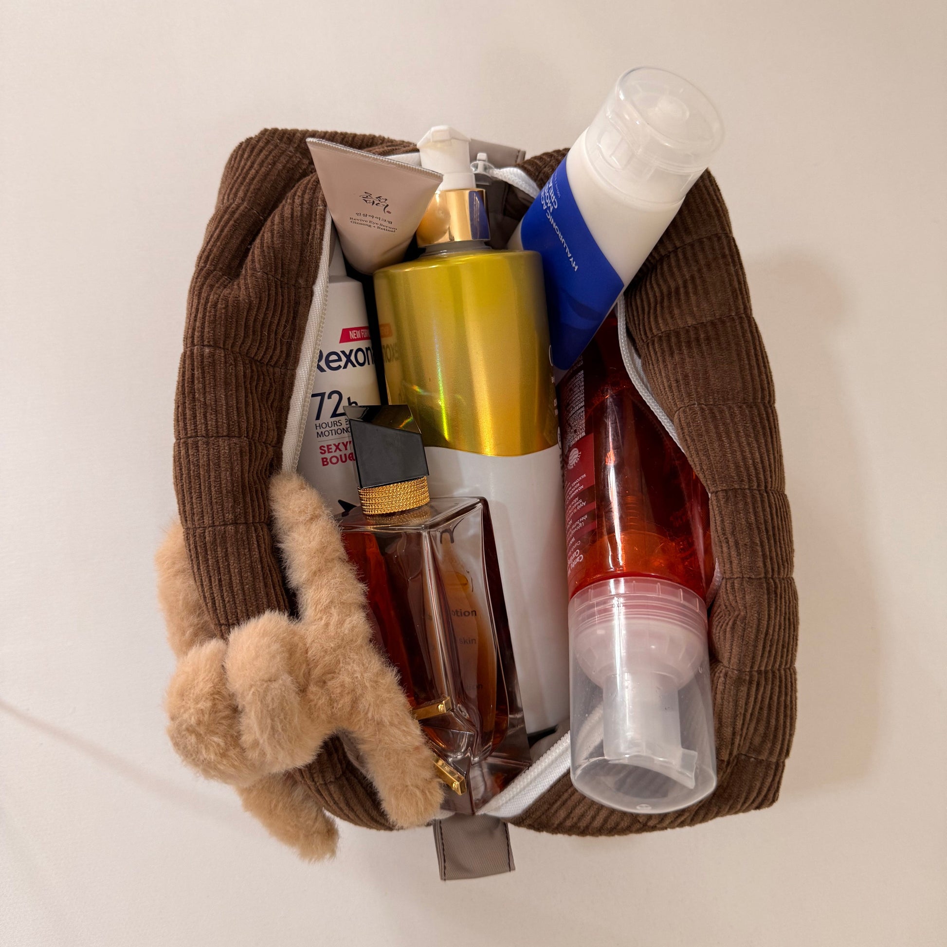 Pouch with various toiletries including bottles and a small teddy bear on a white surface